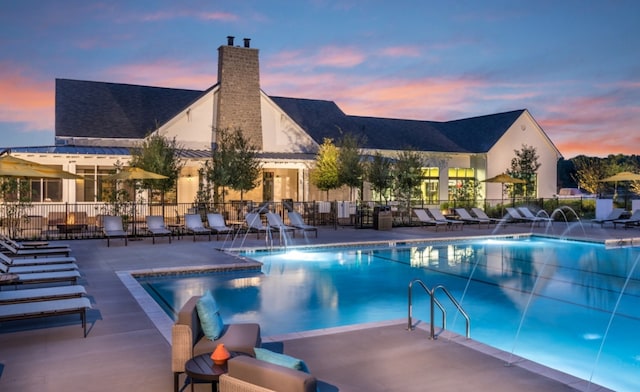 pool at dusk with pool water feature and a patio