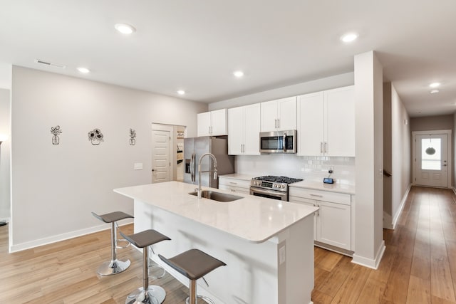 kitchen featuring white cabinets, a center island with sink, stainless steel appliances, and a kitchen bar