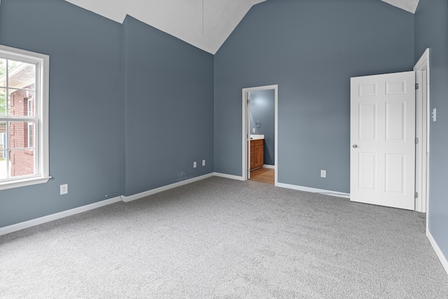 unfurnished bedroom with high vaulted ceiling, connected bathroom, and carpet