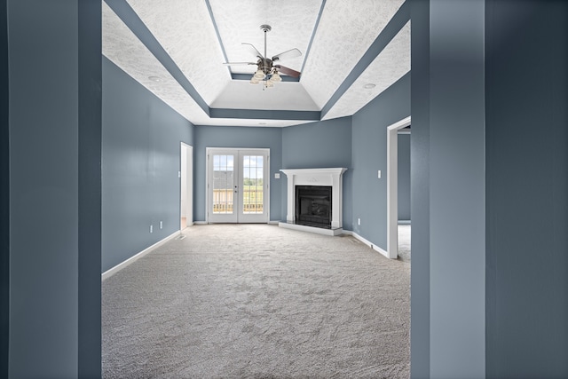 unfurnished living room with a textured ceiling, carpet, a raised ceiling, ceiling fan, and french doors