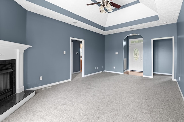 unfurnished living room featuring carpet, vaulted ceiling, ceiling fan, and a raised ceiling