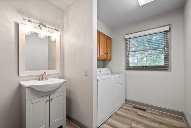 laundry area featuring washing machine and clothes dryer, light hardwood / wood-style flooring, cabinets, and sink