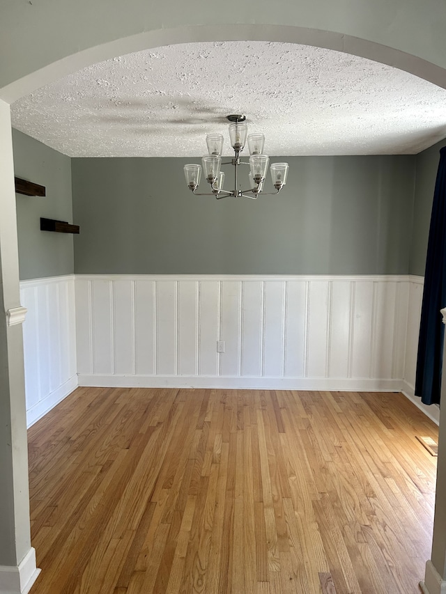 unfurnished room with an inviting chandelier, a textured ceiling, and hardwood / wood-style floors