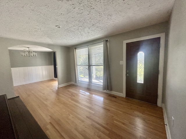 foyer with a notable chandelier, light wood-type flooring, and a textured ceiling