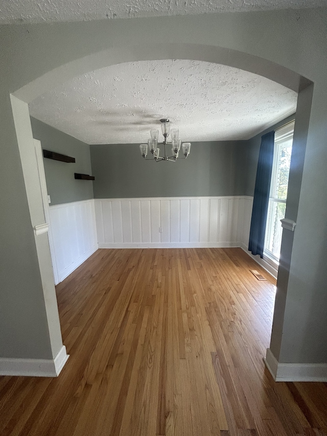 unfurnished dining area with wood-type flooring, a textured ceiling, and an inviting chandelier