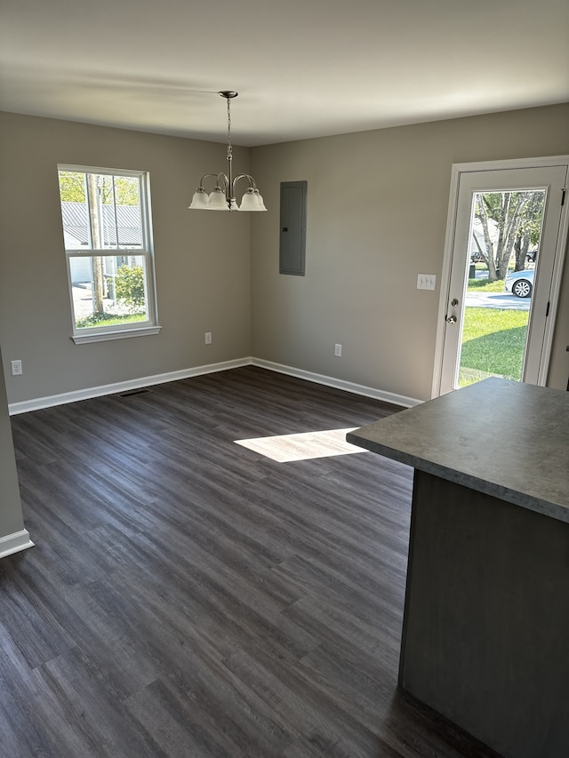 unfurnished dining area featuring dark hardwood / wood-style floors, electric panel, a chandelier, and a wealth of natural light