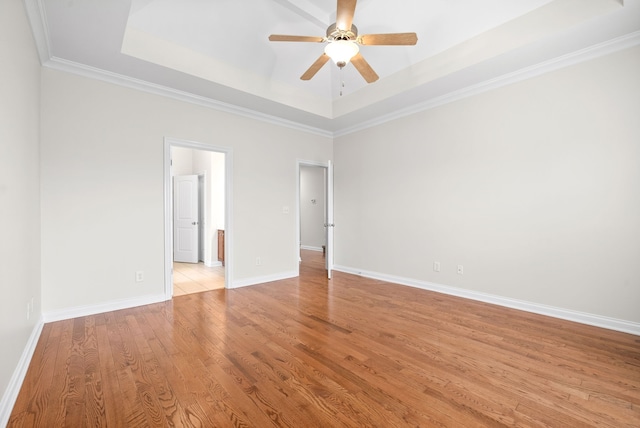 empty room featuring a tray ceiling, light wood-style floors, ornamental molding, a ceiling fan, and baseboards