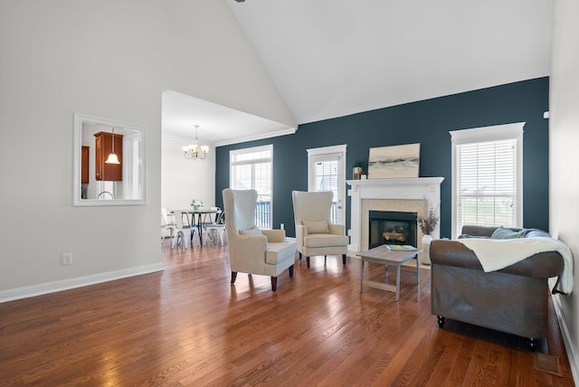 living area with baseboards, wood finished floors, a fireplace, high vaulted ceiling, and a notable chandelier