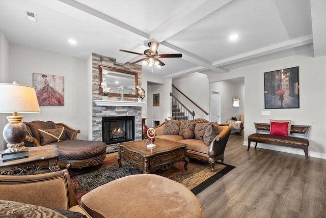 living room featuring ceiling fan, beamed ceiling, hardwood / wood-style floors, and a stone fireplace