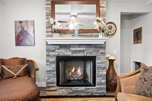 living room with ceiling fan, a stone fireplace, beamed ceiling, and wood-type flooring