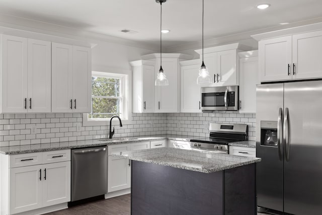 kitchen with hanging light fixtures, white cabinets, a kitchen island, light stone countertops, and stainless steel appliances