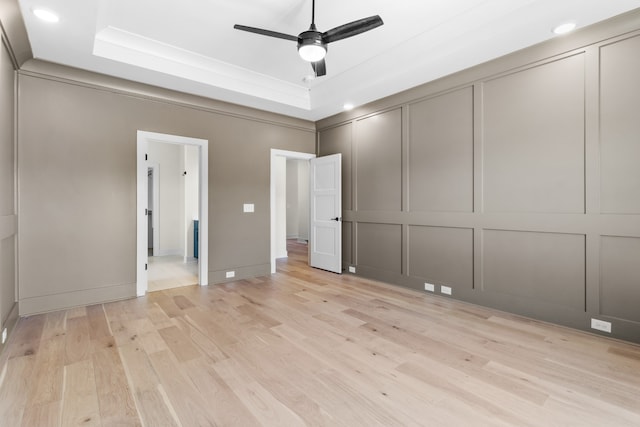 unfurnished bedroom featuring crown molding, ceiling fan, a tray ceiling, light hardwood / wood-style floors, and a closet