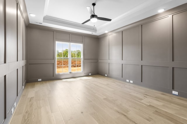 spare room featuring a tray ceiling, ceiling fan, and light hardwood / wood-style flooring