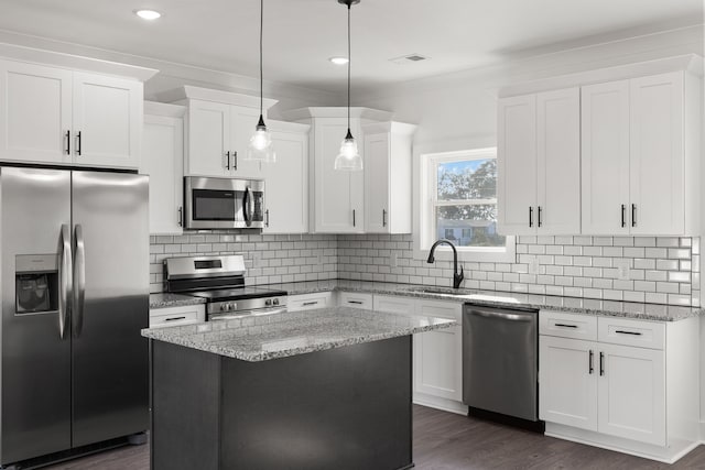 kitchen with pendant lighting, light stone counters, a center island, white cabinets, and appliances with stainless steel finishes