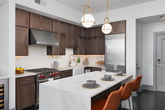 kitchen featuring dark brown cabinets, premium appliances, hanging light fixtures, and tasteful backsplash