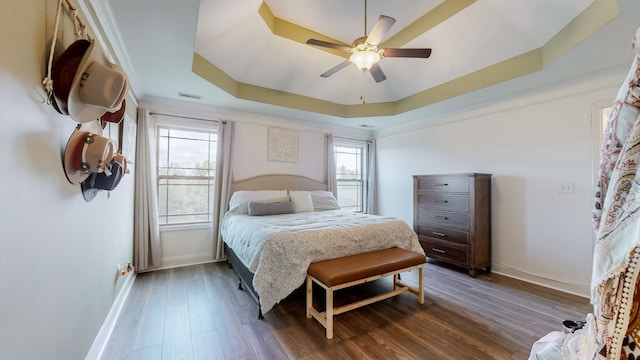 bedroom with ornamental molding, ceiling fan, a raised ceiling, and dark wood-type flooring