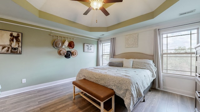 bedroom with ceiling fan, hardwood / wood-style flooring, a tray ceiling, and crown molding