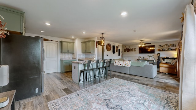 kitchen featuring tasteful backsplash, a kitchen bar, ceiling fan, light hardwood / wood-style flooring, and refrigerator