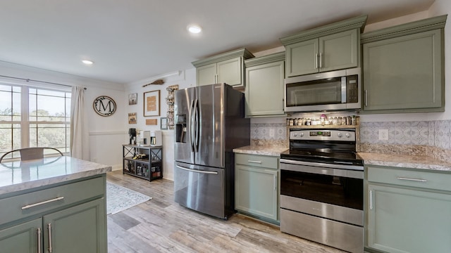 kitchen featuring appliances with stainless steel finishes, light hardwood / wood-style floors, light stone counters, tasteful backsplash, and green cabinets