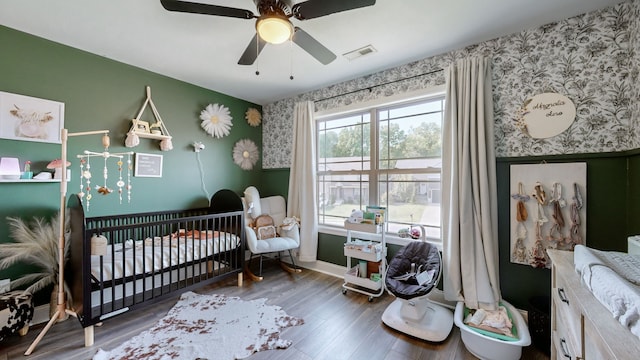 bedroom with ceiling fan, a nursery area, and dark wood-type flooring