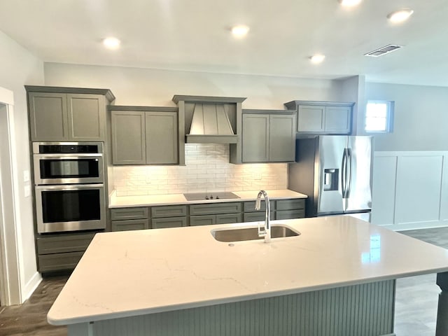 kitchen featuring stainless steel appliances, custom exhaust hood, sink, and a center island with sink