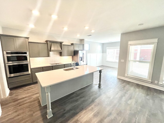 kitchen featuring sink, dark wood-type flooring, a kitchen island with sink, stainless steel appliances, and tasteful backsplash