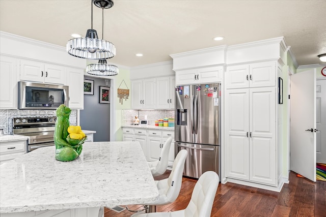 kitchen featuring pendant lighting, white cabinets, ornamental molding, appliances with stainless steel finishes, and dark hardwood / wood-style floors