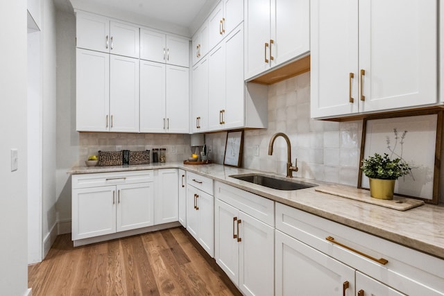 kitchen with light wood-type flooring, white cabinetry, light stone counters, and sink