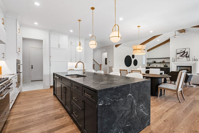 kitchen featuring an island with sink, hanging light fixtures, sink, lofted ceiling with beams, and light wood-type flooring