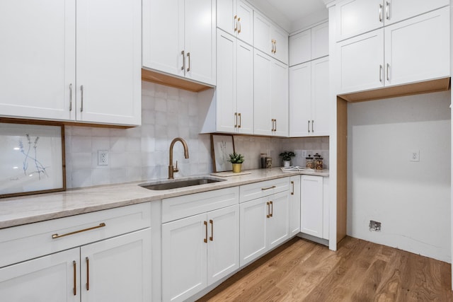 kitchen with light wood-type flooring, sink, white cabinets, backsplash, and light stone countertops