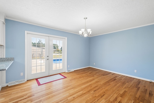 unfurnished dining area featuring a textured ceiling, ornamental molding, light hardwood / wood-style flooring, and french doors