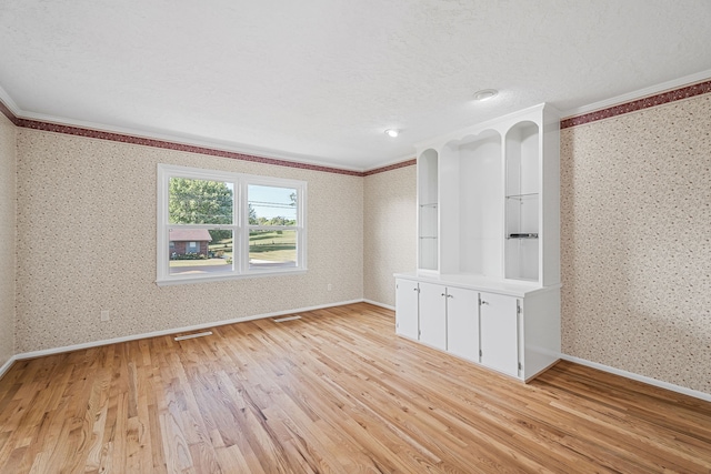 empty room with a textured ceiling, ornamental molding, and light hardwood / wood-style flooring