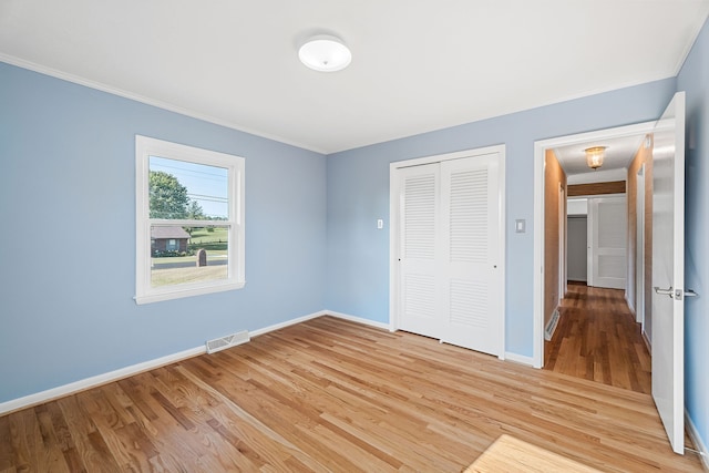 unfurnished bedroom with ornamental molding, light wood-type flooring, and a closet