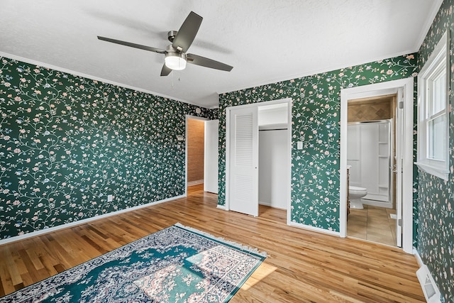 bedroom with ceiling fan, hardwood / wood-style floors, a textured ceiling, a closet, and ensuite bathroom