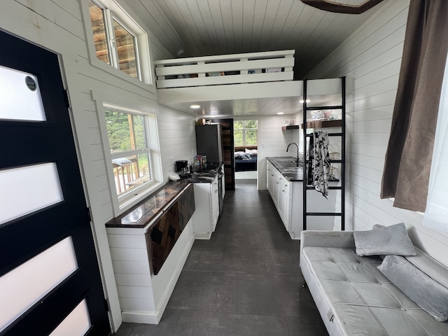 kitchen with wooden ceiling, wood walls, sink, and white cabinets