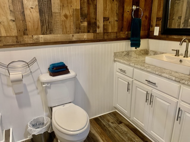 bathroom with wood-type flooring, wooden walls, vanity, and toilet