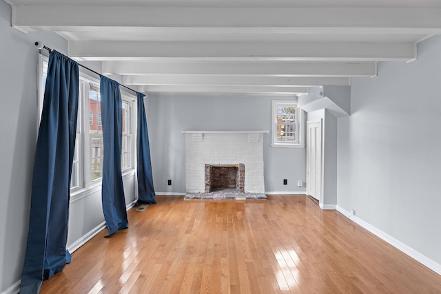 unfurnished living room with a brick fireplace, beamed ceiling, and light hardwood / wood-style flooring