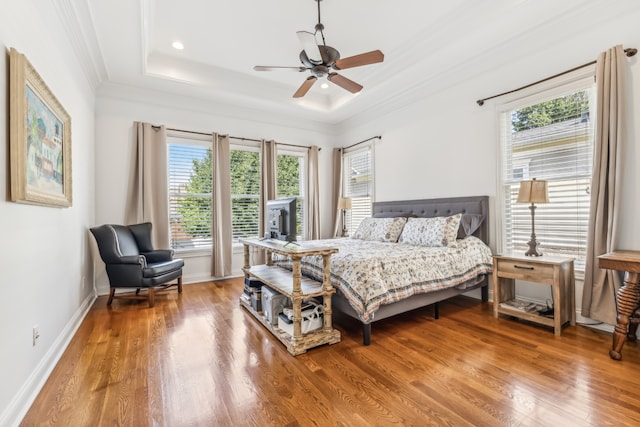 bedroom with wood-type flooring, ornamental molding, ceiling fan, and a raised ceiling