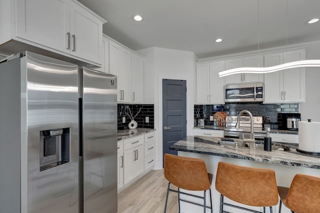 kitchen featuring appliances with stainless steel finishes, white cabinetry, stone counters, and tasteful backsplash