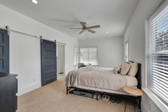 carpeted bedroom with a barn door and ceiling fan