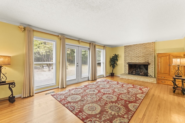 living room with light hardwood / wood-style floors, a brick fireplace, a textured ceiling, french doors, and ornamental molding