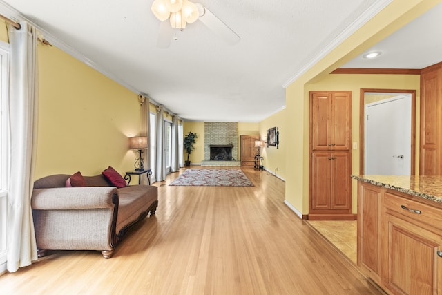 living room featuring ceiling fan, light wood-type flooring, a fireplace, and ornamental molding