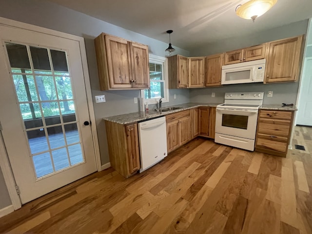 kitchen featuring light stone counters, sink, hanging light fixtures, light hardwood / wood-style flooring, and white appliances