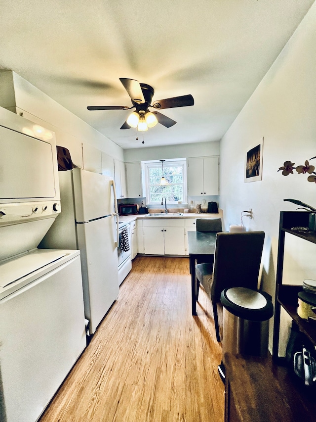 kitchen with white cabinets, white appliances, sink, light hardwood / wood-style flooring, and stacked washing maching and dryer