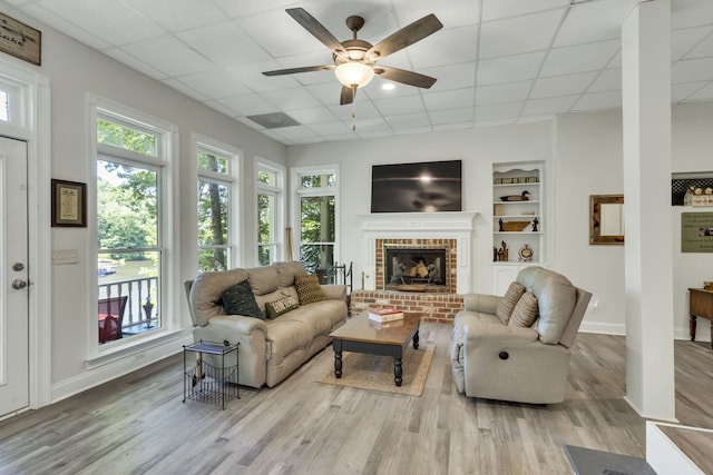 living room featuring wood-type flooring, ceiling fan, a fireplace, and a paneled ceiling