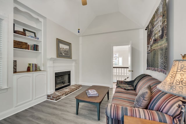 living room featuring a brick fireplace, wood-type flooring, vaulted ceiling, and built in shelves