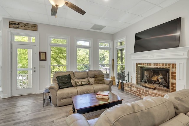 living room featuring a brick fireplace, a paneled ceiling, light hardwood / wood-style floors, and ceiling fan