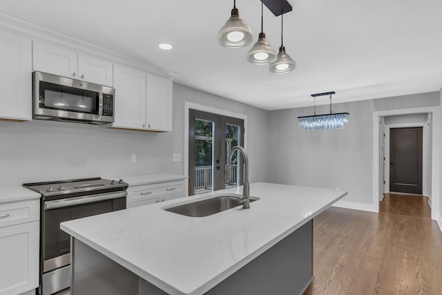 kitchen with appliances with stainless steel finishes, a center island with sink, hanging light fixtures, and white cabinets