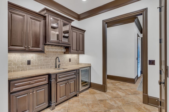 kitchen with light stone counters, ornamental molding, sink, dark brown cabinets, and beverage cooler