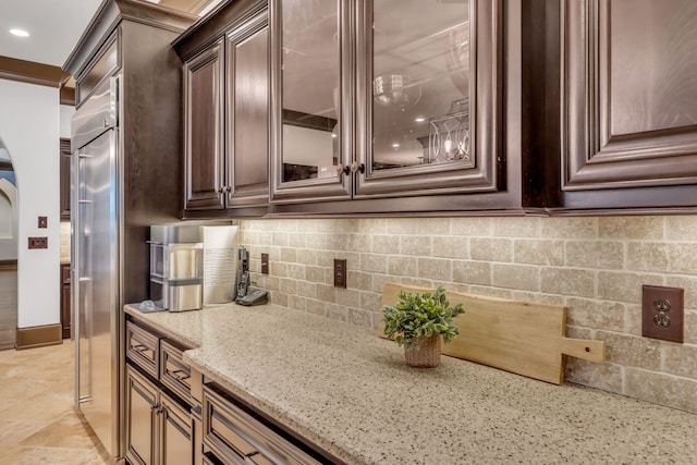 kitchen featuring light stone counters, dark brown cabinetry, and backsplash